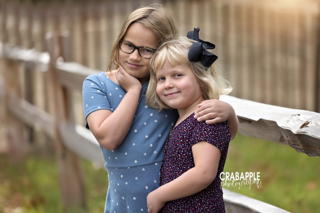 Two sisters hug and smile at camera during family photo session