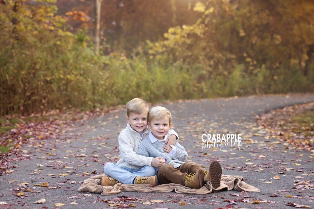 Two brothers sitting together surrounded by colorful autumn leaves during North Shore family portraits