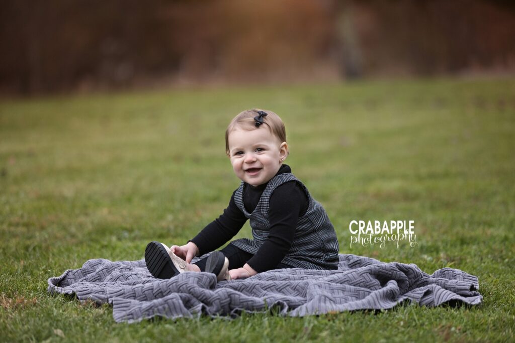 Baby photos outside in the fall in Tewksbury MA One year old girl sitting on blanket in the grass during fall family portrait session near Tewksbury MA
