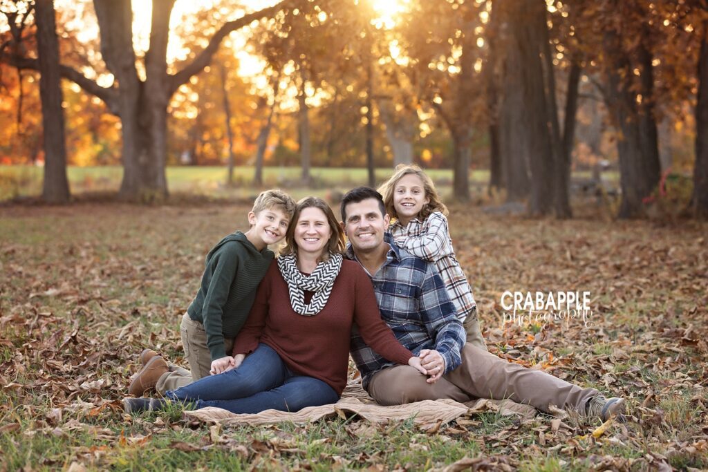 Posed portrait of a family of four sitting on a blanket in the fallen autumn leaves during their portrait session