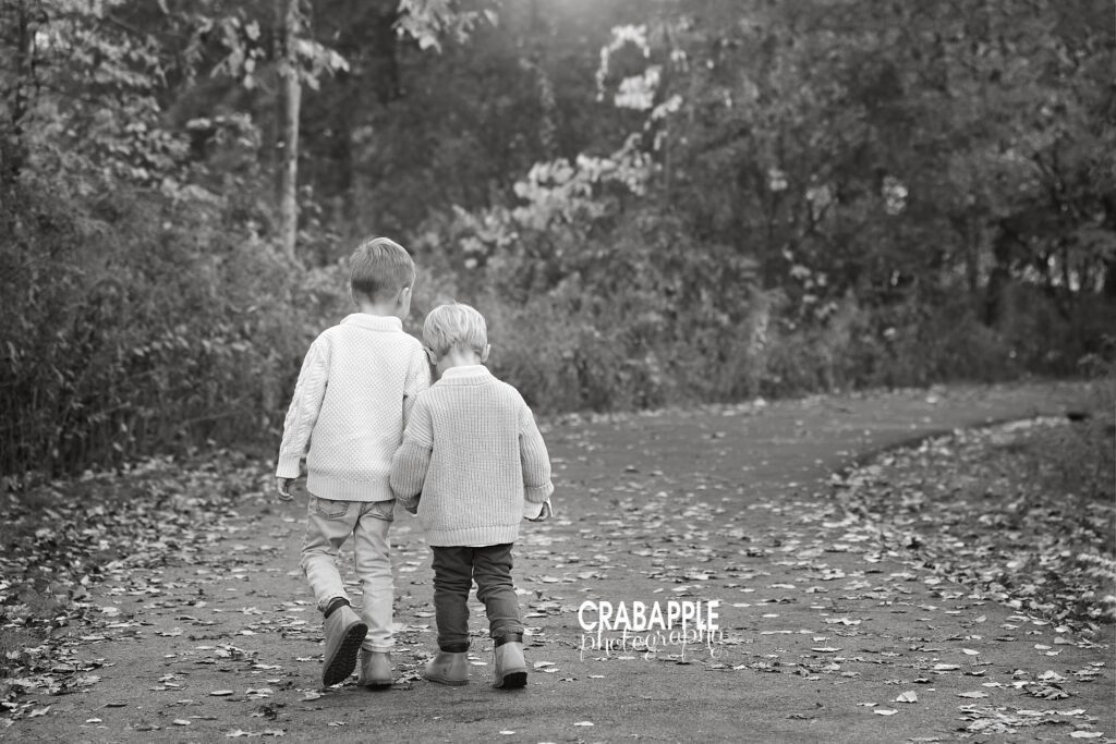 Black and white candid sibling photo of two young brothers walking hand in hand during fall session in Lynnfield