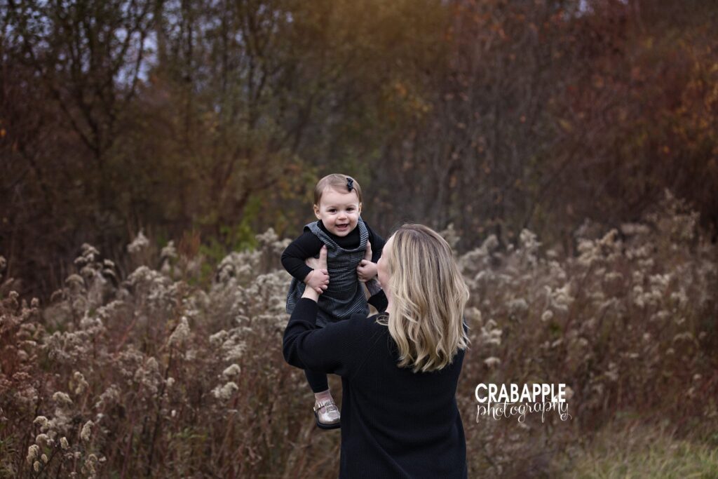 Mom and daughter portraits in Massachusetts fall session Mother lifting baby girl in the air in autumn sunlight