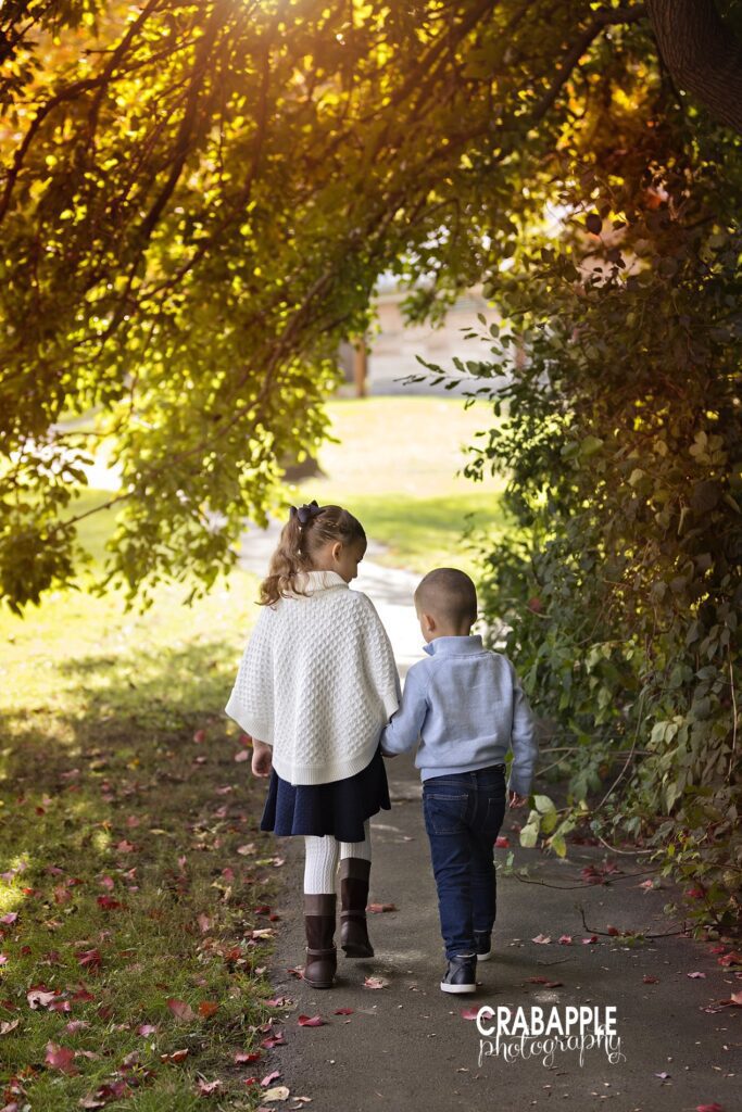 A photo of two siblings walking away from the camera in adorable fall outfits using neutral shades of ivory, navy, and gray