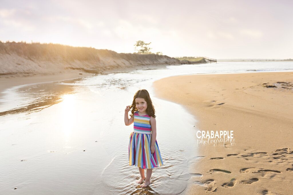 Soft light portrait of child standing near ocean waves at sunset
