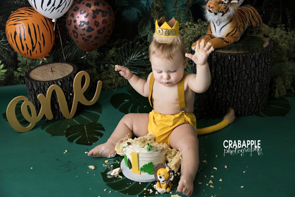 Jungle Cake Smash Setup Cake smash setup with dark green backdrop, animal print balloons, and stuffed tiger