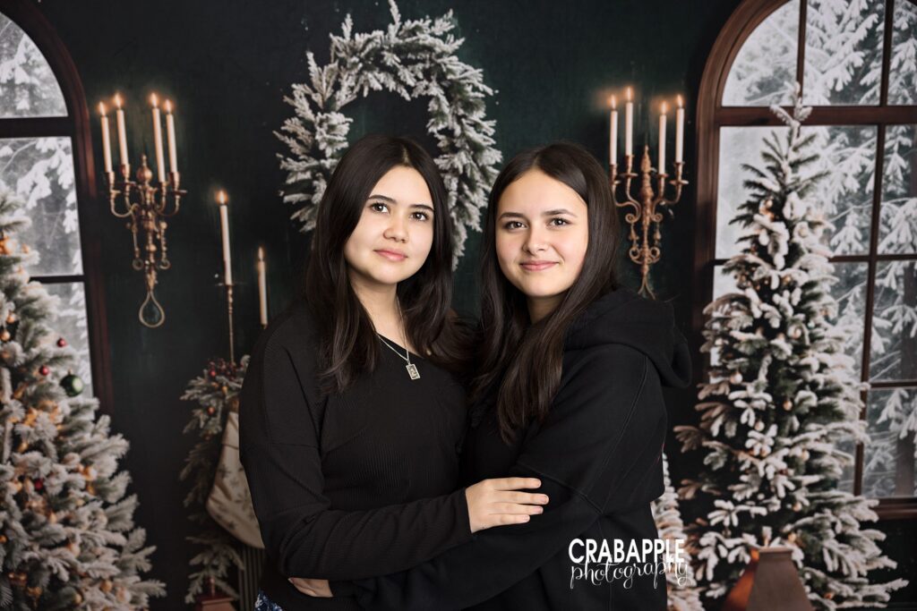 Two preteen sisters in casual black clothing hug one another during holiday photos north of Boston