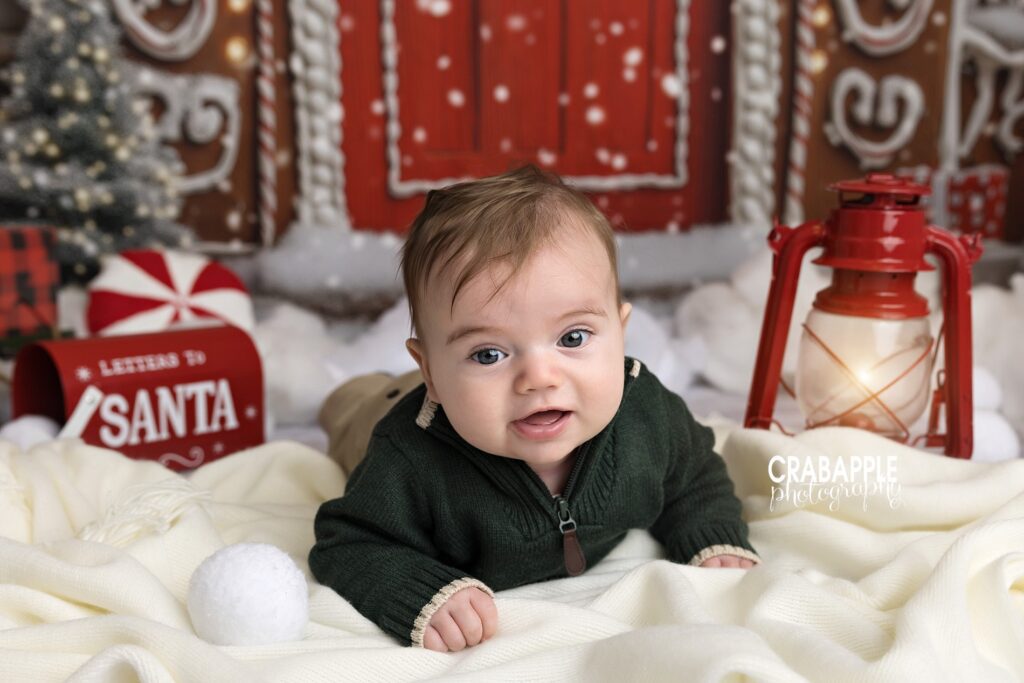Baby’s first Christmas photo session | Christmas newborn photography ideas Smiling baby on tummy surrounded by glowing lantern and holiday props during baby’s first Christmas photo session.