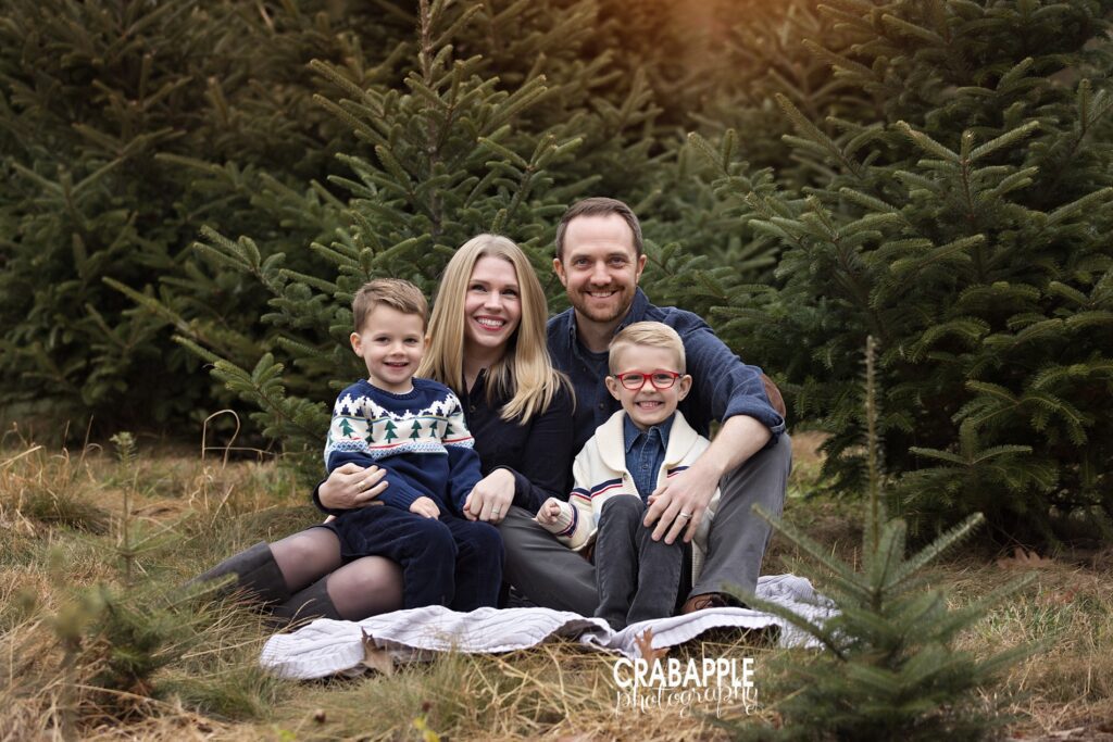 Family of four sits on a blanket surrounded by evergreen pine trees during outdoor family photo session