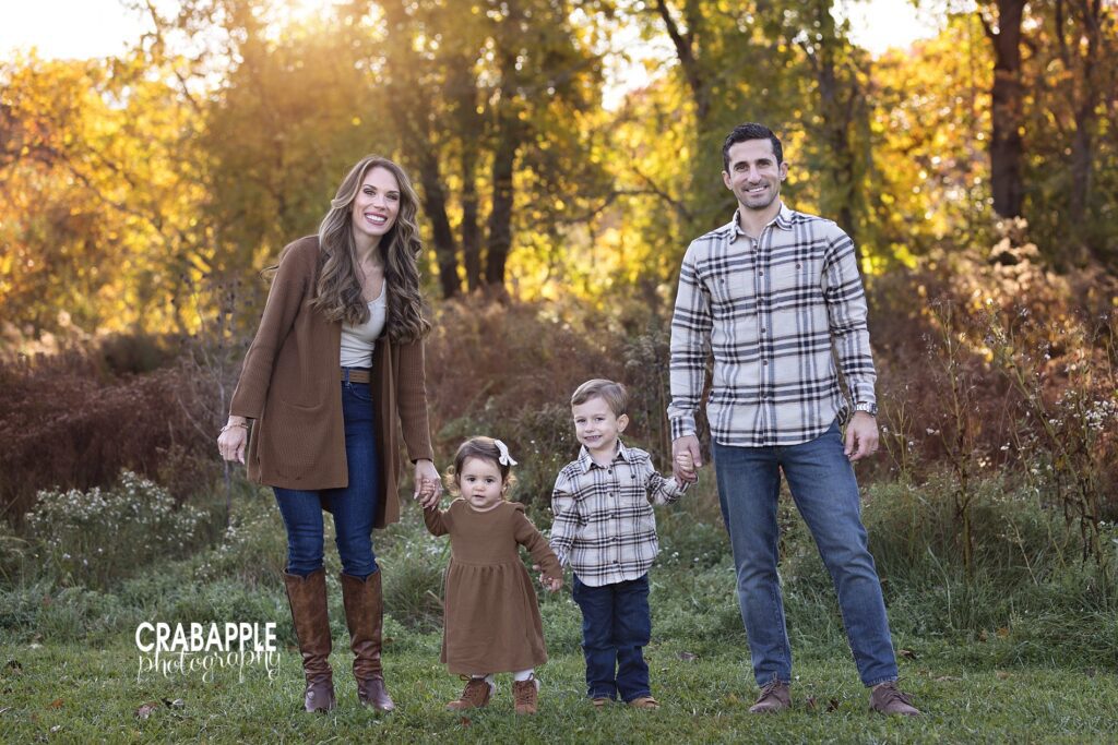 Family posing in front of golden light and trees during North Shore MA fall portraits
