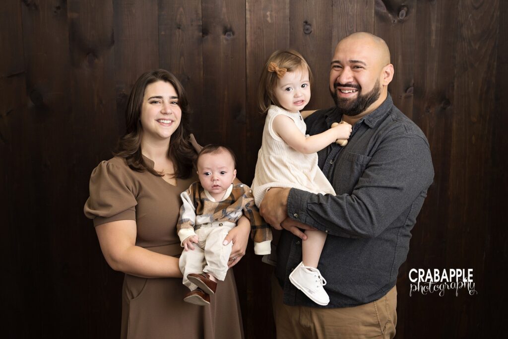 Rustic indoor fall family photo in Massachusetts studio. Rustic fall family photo in studio featuring mom, dad, toddler daughter, and baby boy in neutral fall tones.