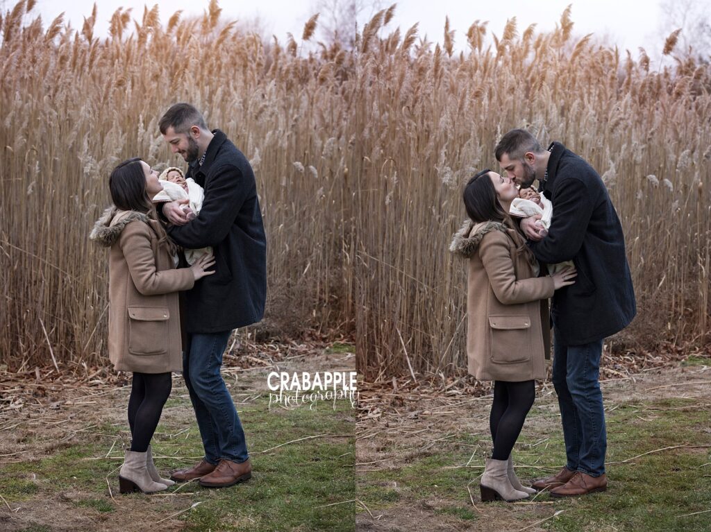 Mom and dad standing close together holding baby near tall golden reeds
