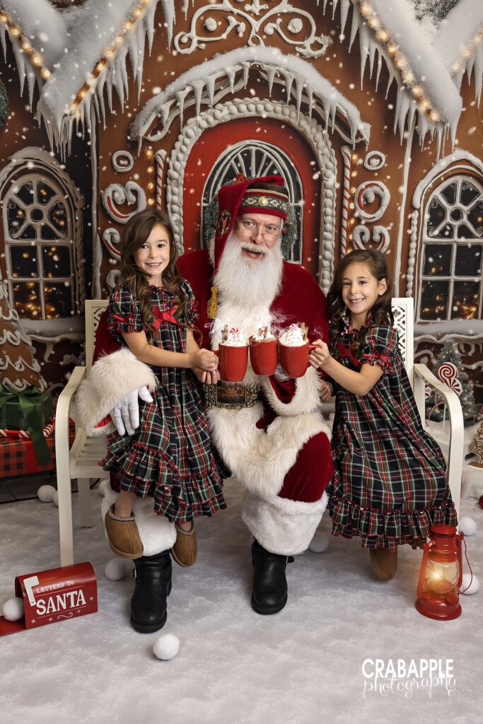 2024 Santa mini session North of Boston with two sisters clinking cocoa mugs with Santa.
