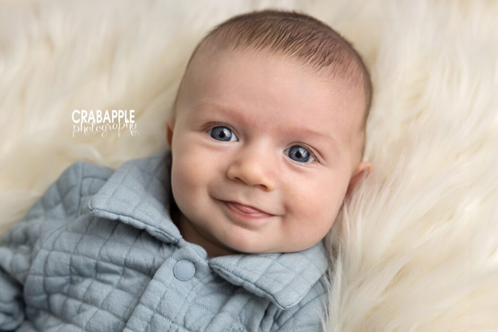 Winter Baby Portraits Three month old baby smiling on white fur blanket during cozy winter studio photoshoot