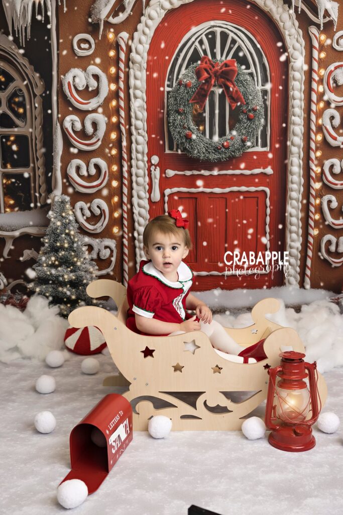 Toddler girl sits in wooden sleigh during holiday mini session in Andover MA
