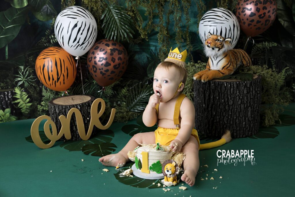Studio Cake Smash Session for Boys Baby with lion tail outfit sitting in front of intricate set design and eating cake during jungle themed cake smash session