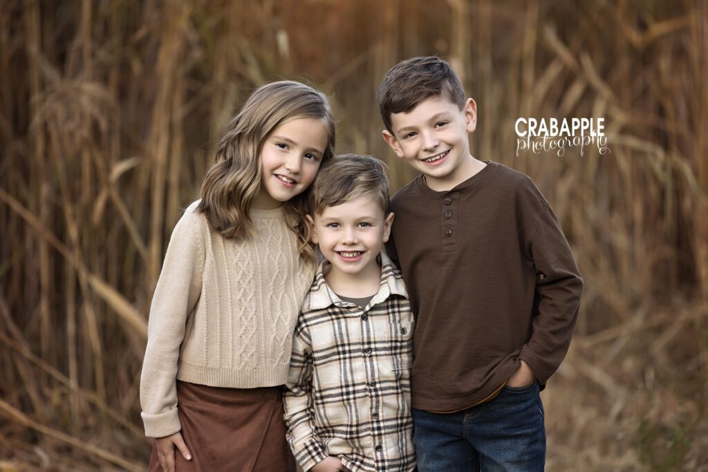 Three siblings in coordinating neutral outfits pose together at park near Andover MA