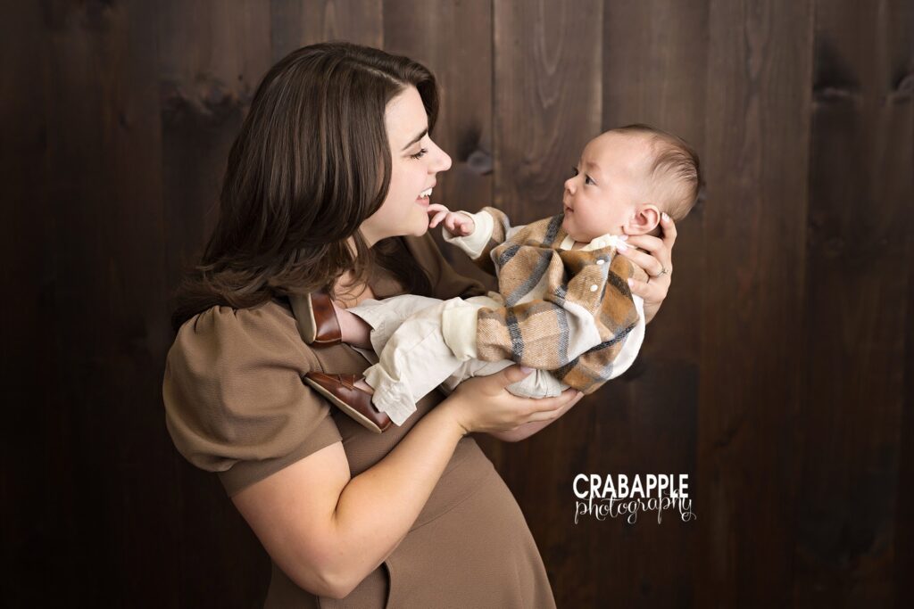 Cozy mother and baby portrait during indoor fall family session. Cozy indoor fall photo of mother cradling 3-month-old baby in rustic studio setting.