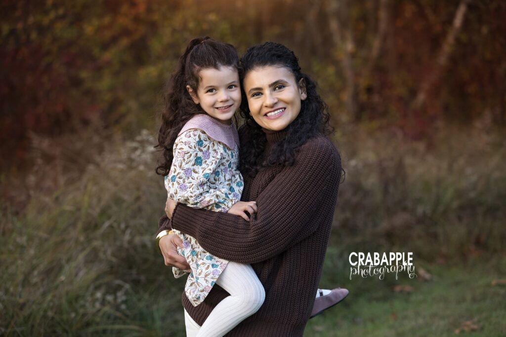 Mom holding her young daughter close during cozy fall park session
