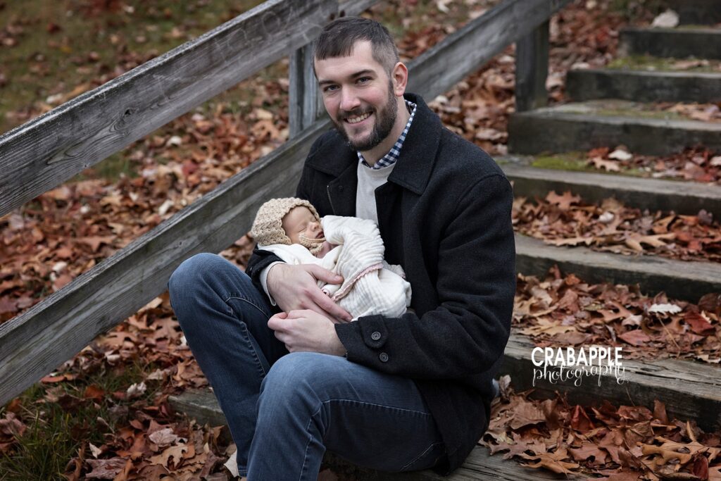 Dad smiling while cradling baby girl wrapped in knit blanket during December photo session
