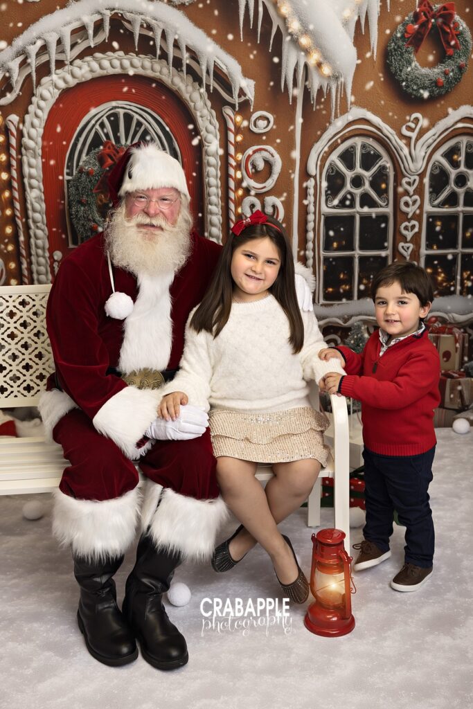 Santa sits with older sister while toddler brother stands next to them 