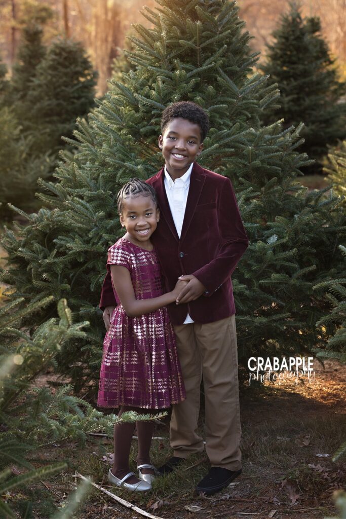 Brother and sister in formal outfits pose for holiday photos at the tree farm