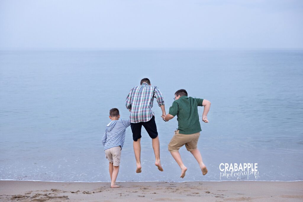 Three siblings holding hands and jumping by the ocean in North Shore MA
