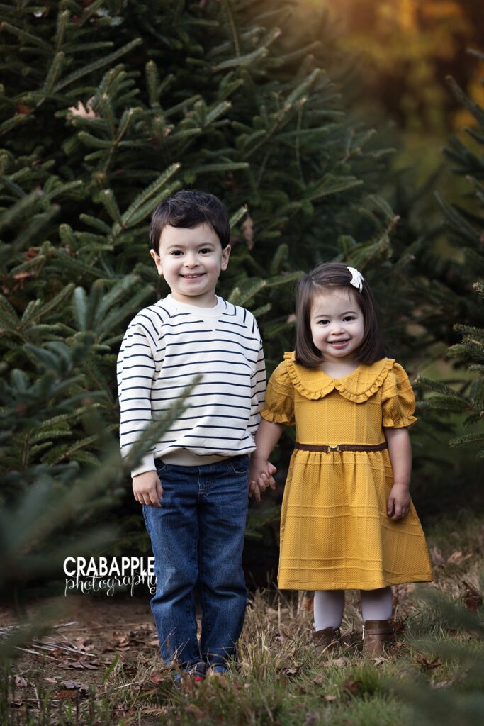 Brother and sister pose together in front of Christmas tree outside for holiday photos