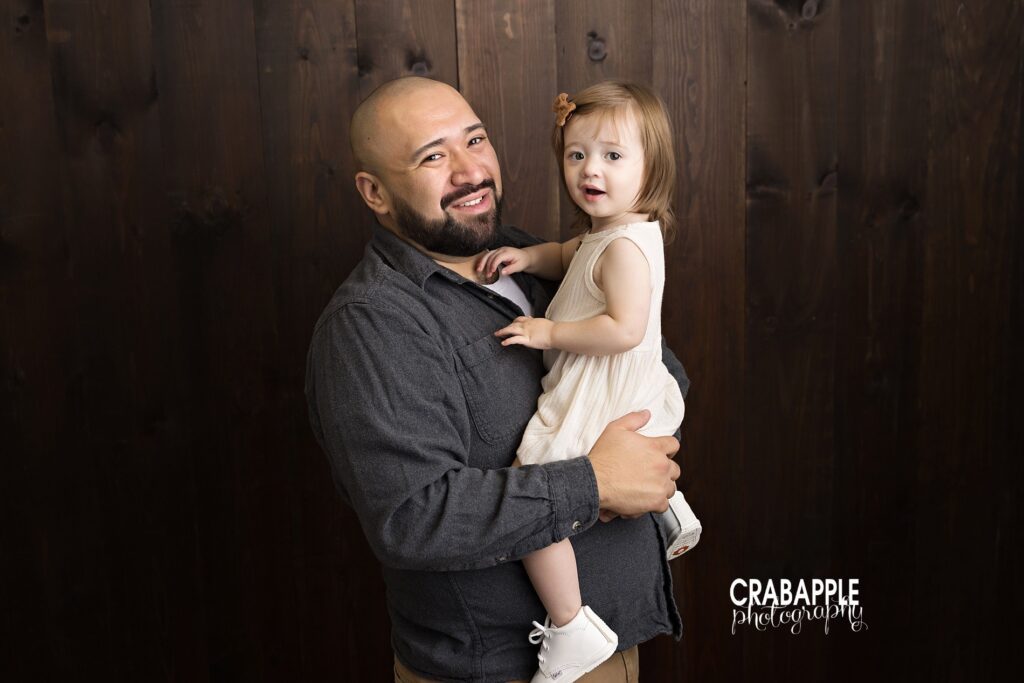 Father holding toddler daughter in cozy indoor fall family session with warm tones.
