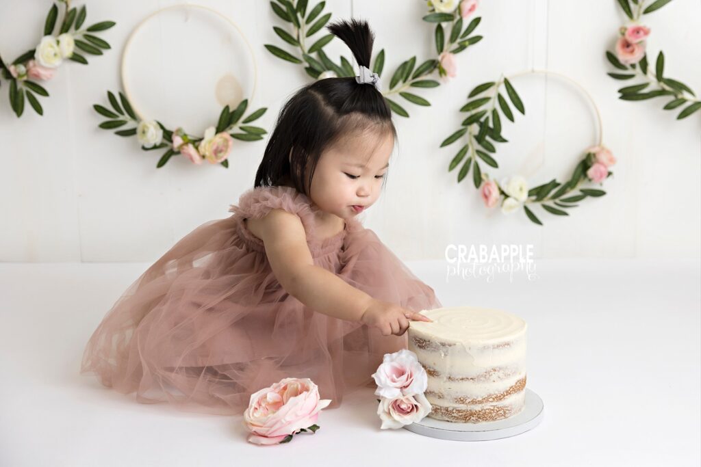 Portrait of 1 year old baby girl sneaking some frosting from her cake during Quincy area cake smash portrait session