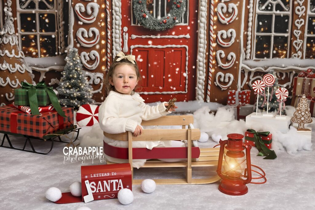Toddler girl sitting in a holiday sleigh during timeless Christmas studio portraits
