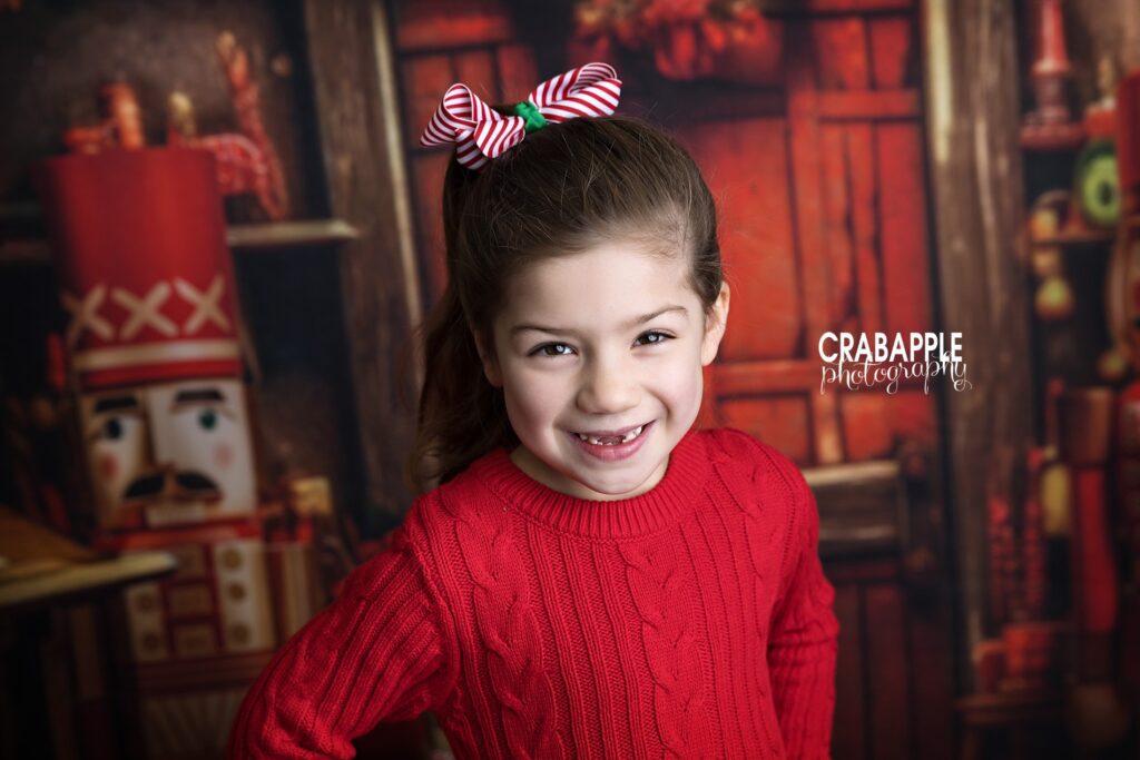Solo portrait of a 5 year old girl in red sweater with bow in her hair during a family Christmas portrait session north of Boston