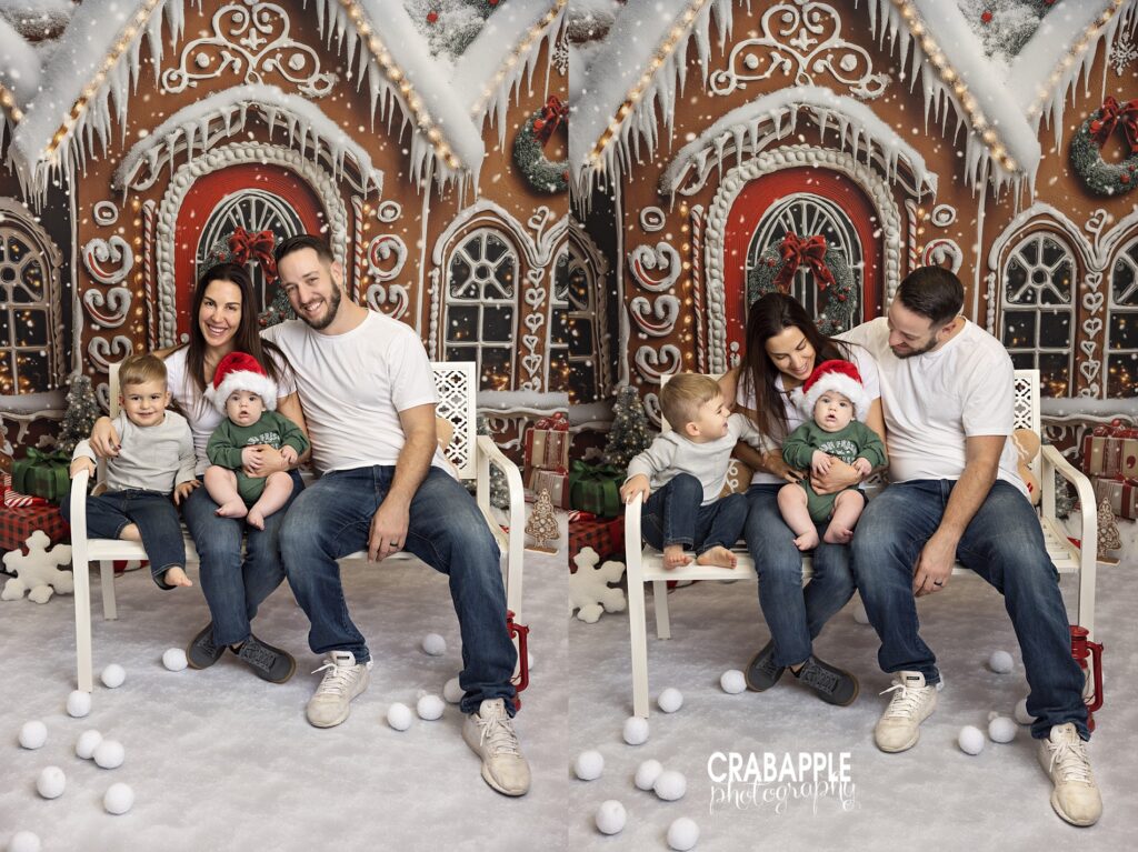 Parents sitting with two young boys in front of a gingerbread house Christmas backdrop.
