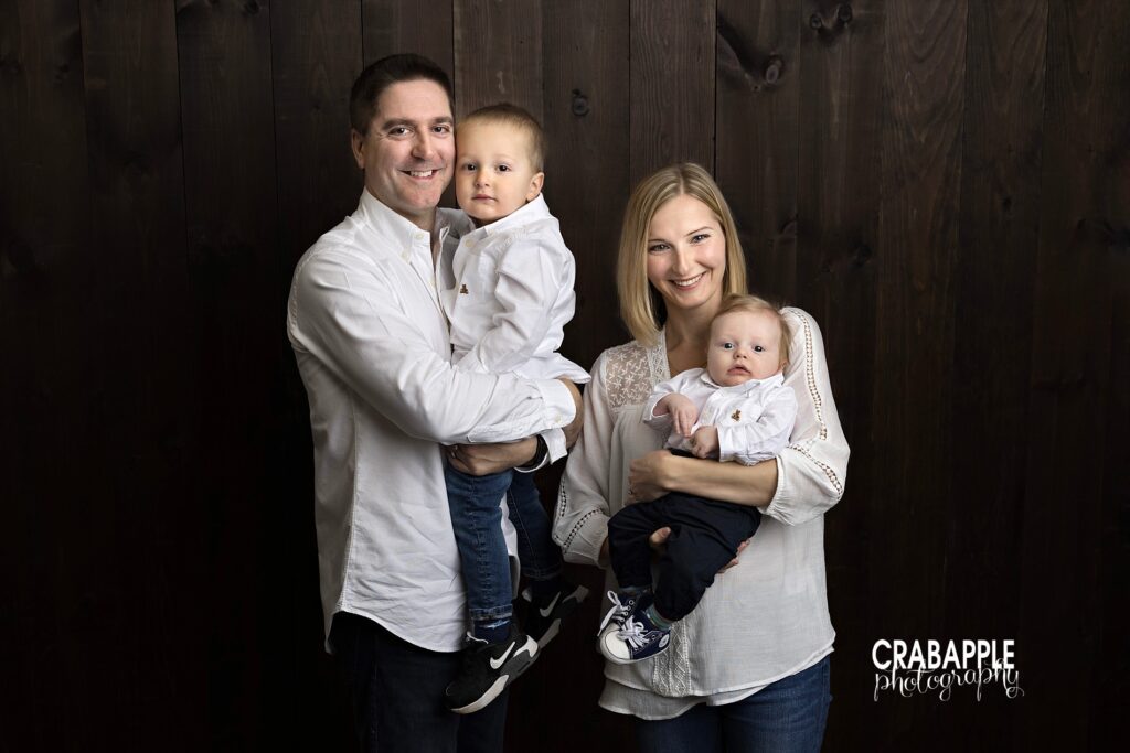 Mom dad toddler and newborn baby posed together in studio family portrait
