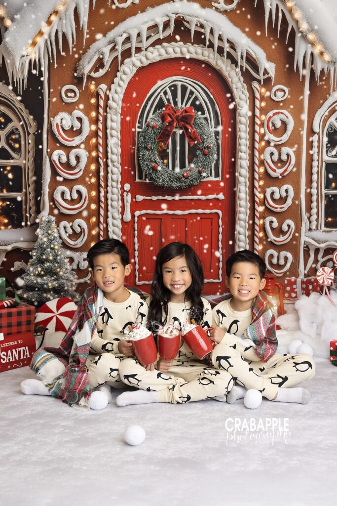 Three siblings wearing matching pajamas and sharing hot cocoa during cozy Christmas studio portrait session