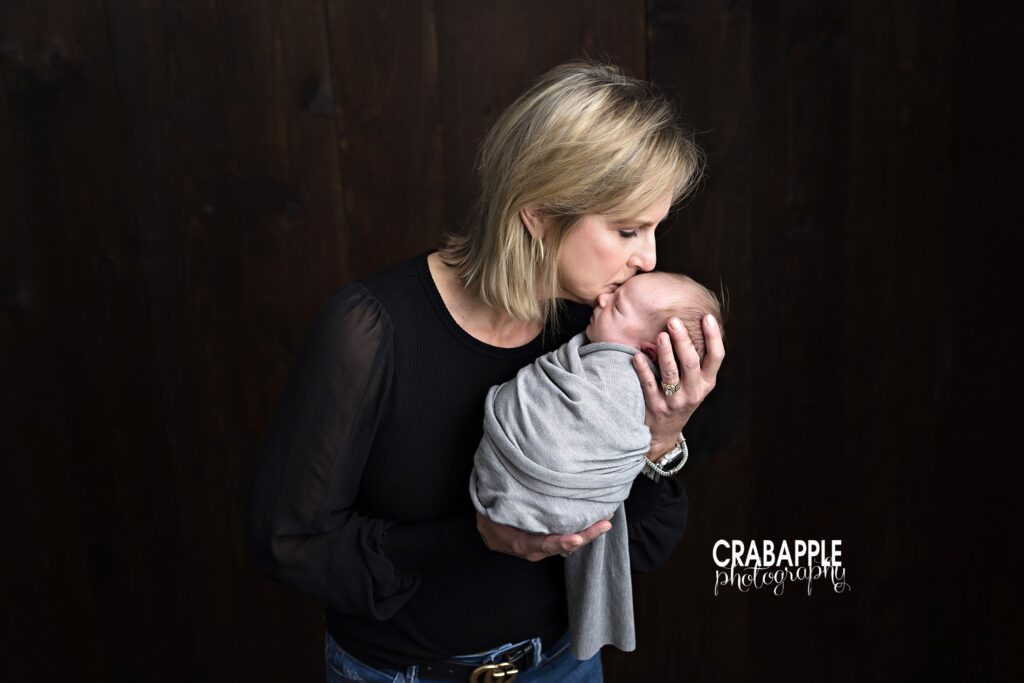 Grandmother holding newborn grandson close to her chest and giving him a sweet kiss during Dorchester MA newborn portrait session