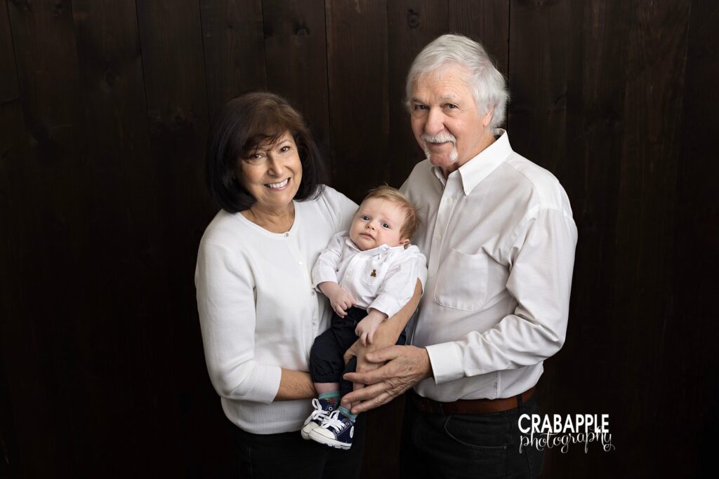 Grandmother and grandfather holding newborn baby boy in timeless portrait
