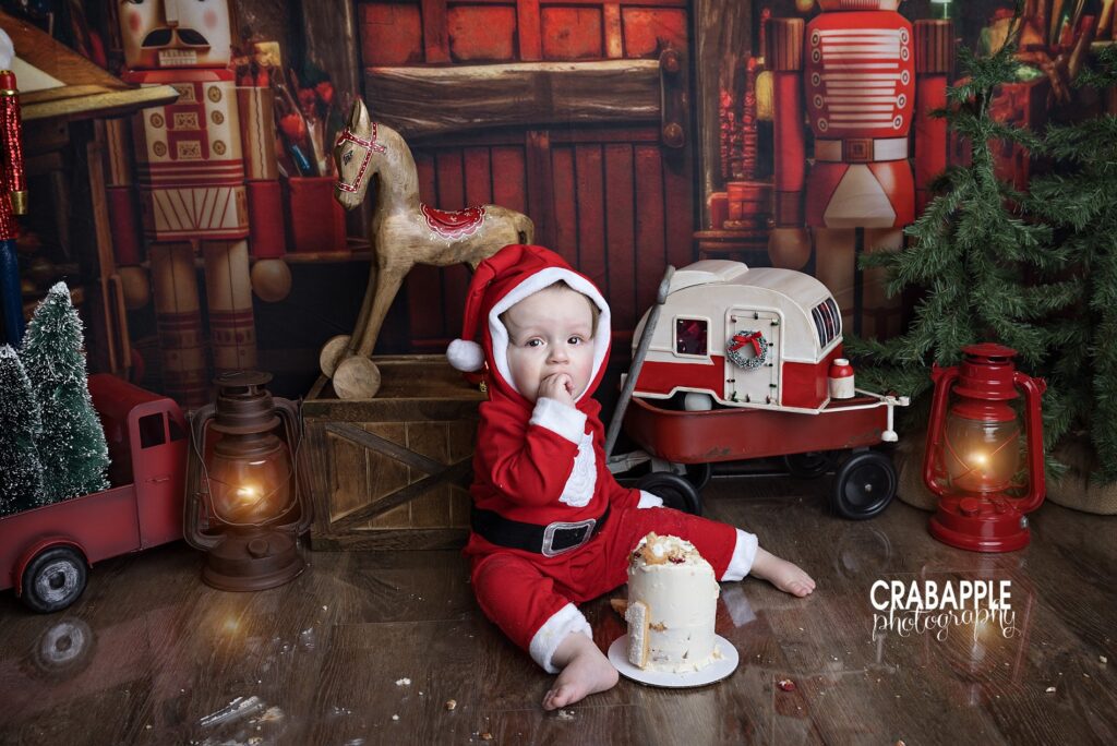 1 year old boy in Santa suit eating cake during his Christmas themed cake smash