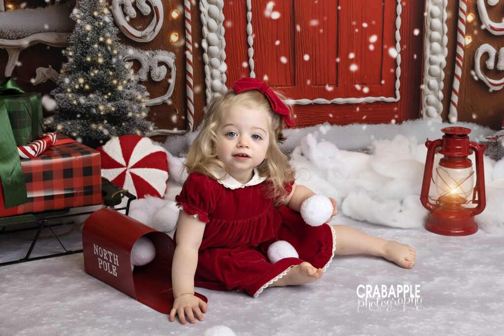 Toddler girl wearing classic red Christmas dress in timeless holiday studio portrait with snowball props