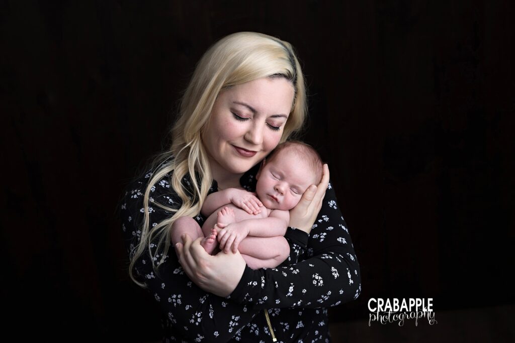 Mom smiling down at newborn baby on black backdrop | Family newborn portraits Massachusetts
