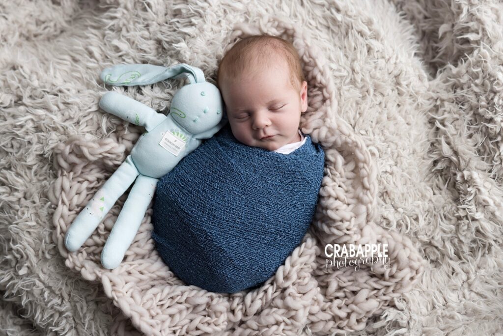 Newborn swaddled in blue blanket with stuffed animal on brown fur | North Shore MA newborn photographer

