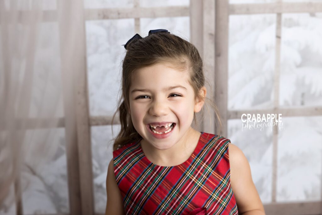 5-year-old girl in red plaid dress smiles for the camera in front of a winter window set design