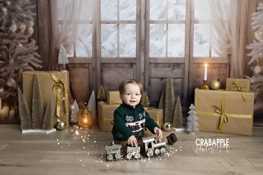 1 year old boy smiles for the camera while playing with a silver toy train, with digitally added sparkles and glowing lights surrounding him