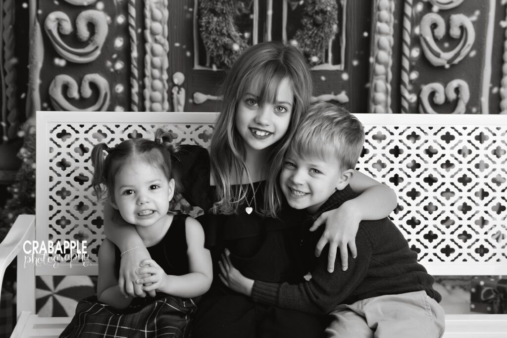 Black and white Christmas studio photo of three siblings in timeless portrait moment