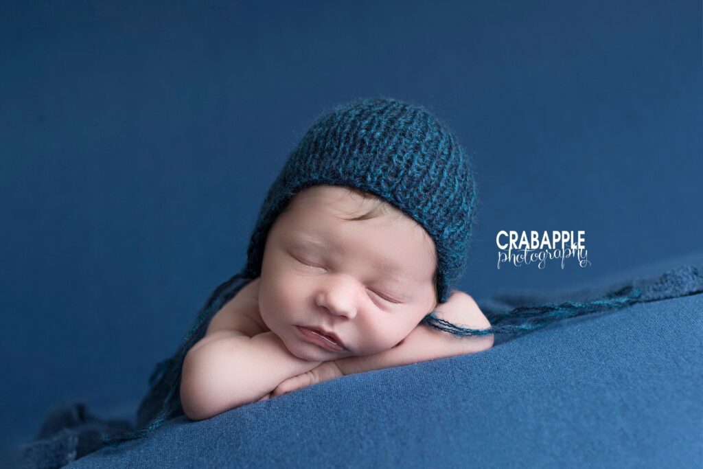 Newborn baby boy resting chin on hands with blue background studio setup
