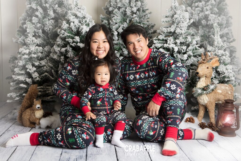Family of three smiling in matching Christmas pajamas on a bright white backdrop.
