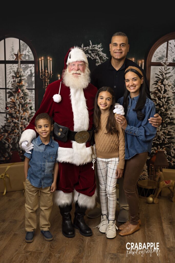 Family of four stand with Santa Claus and smile at the camera
