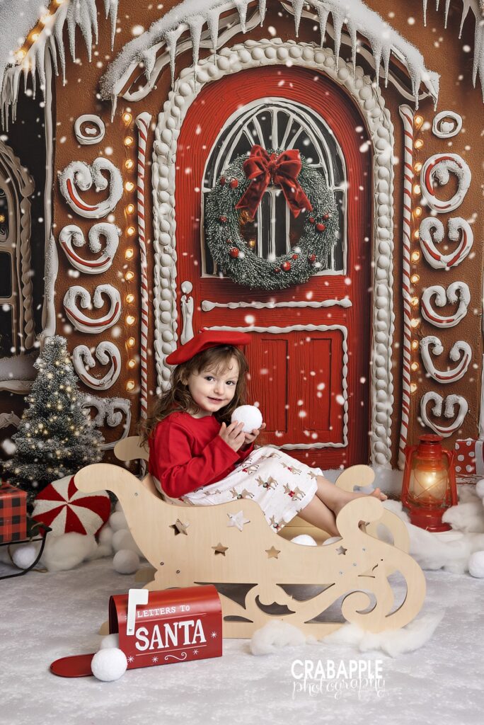 Young girl sitting in a wooden sleigh holding a snowball in a holiday studio