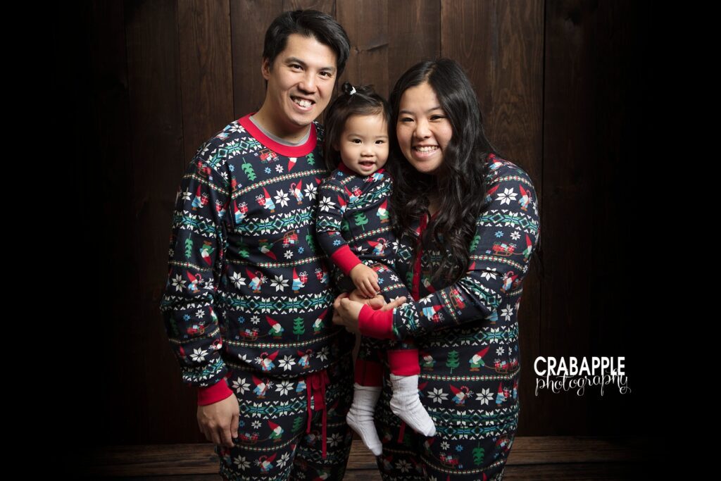 Cozy family holiday portrait with matching Christmas pajamas on a darker studio backdrop.