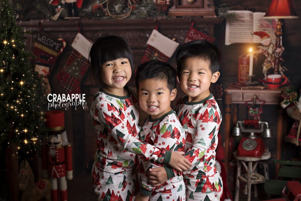 Three siblings hugging in matching festive Christmas pajamas during holiday portraits.