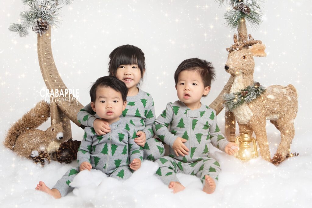 Three siblings posing together in matching gray Christmas tree pajamas.